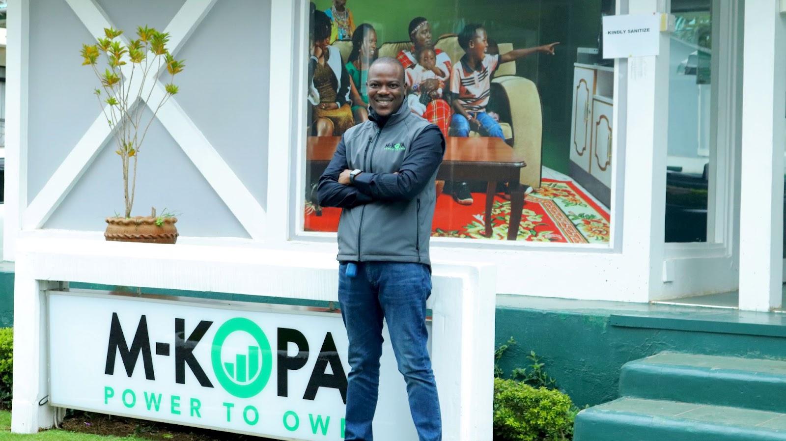 Babajide Duroshola standing in front of M-KOPA's logo